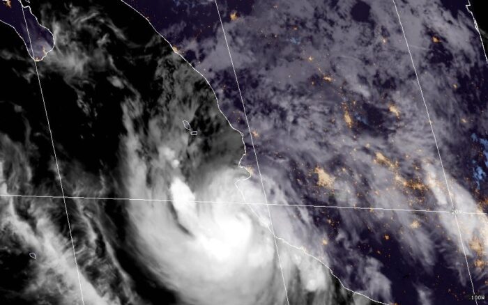 Costa del Pacífico mexicano preparándose para un huracán: oleaje, palmeras al viento, comercios con ventanas protegidas